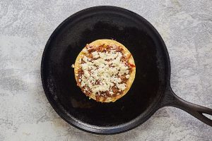 Top down view of a tortilla shell filled with Birria meat and cheese in a cast iron skillet - Hostess At Heart