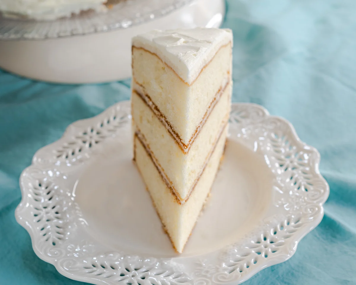 A slice of layered homemade vanilla cake from scratch sitting on a plate. Hostess At Heart