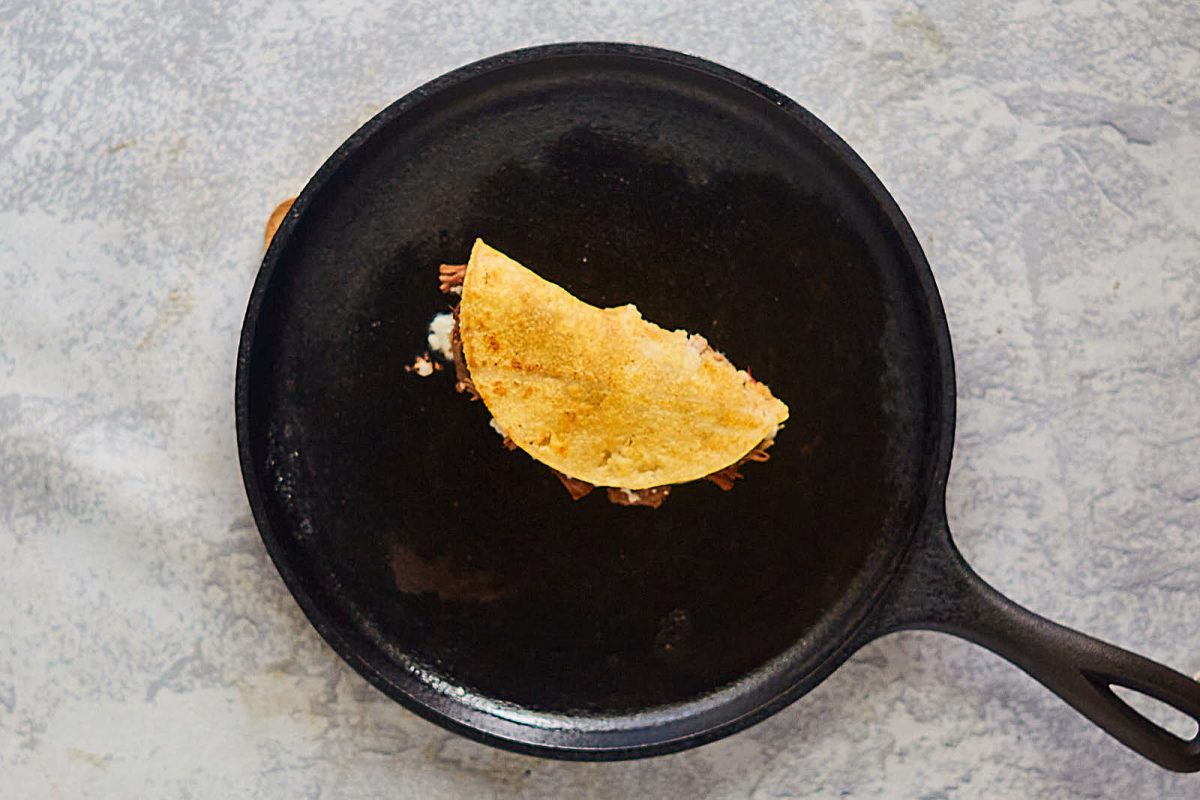 Top down view of a birtia taco sitting in the middle of a cast iron skillet