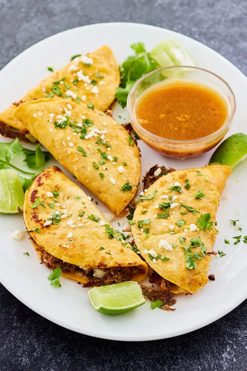 Angled view of birris tacos on a plate topped with chopped cilantro and lime wedges - Hostess At Heart