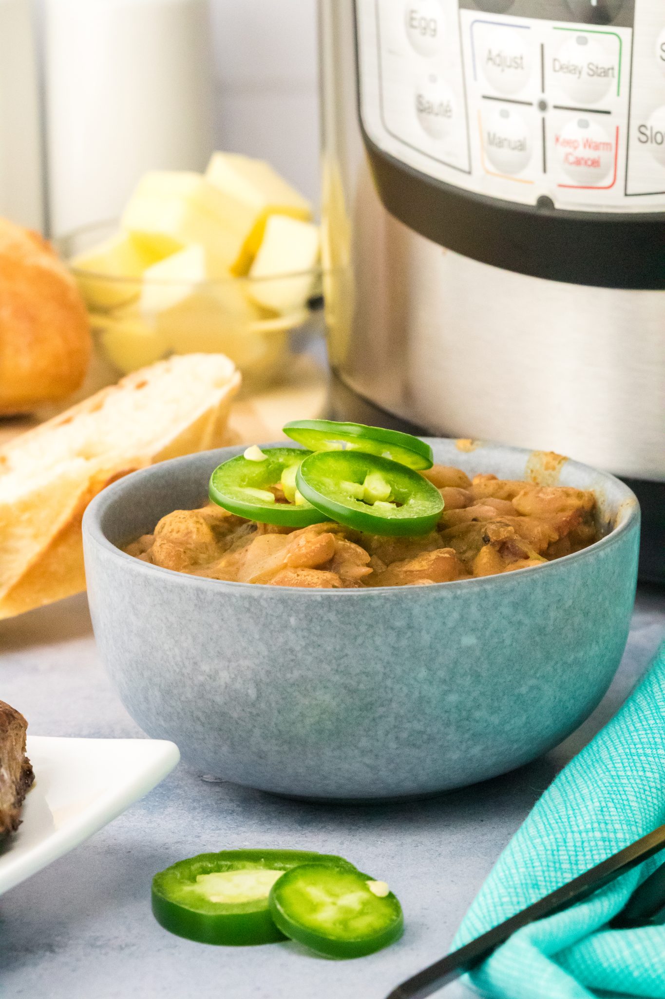 Sideview of a bowl filled with cooked pinto beans topped with slices of jalapenos - Hostess At Heart