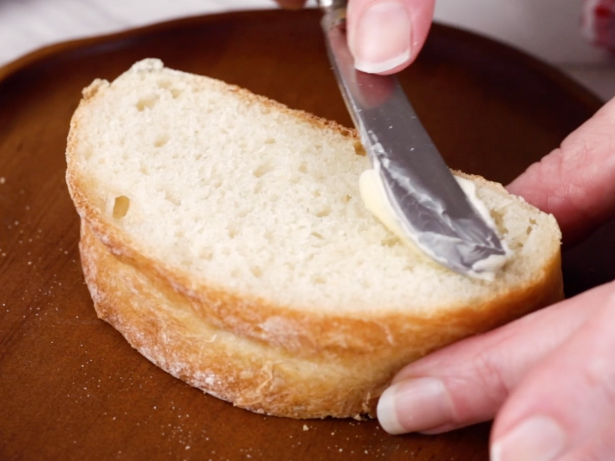 A slice of homemade bread being buttered on a cutting board - Hostess At Heart