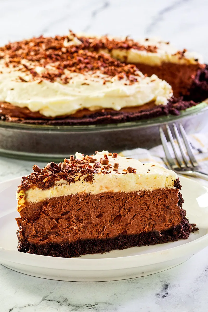 Sideview of a slice of chocolate French Silk Pie with the whole pie in the back - Hostess At Heart