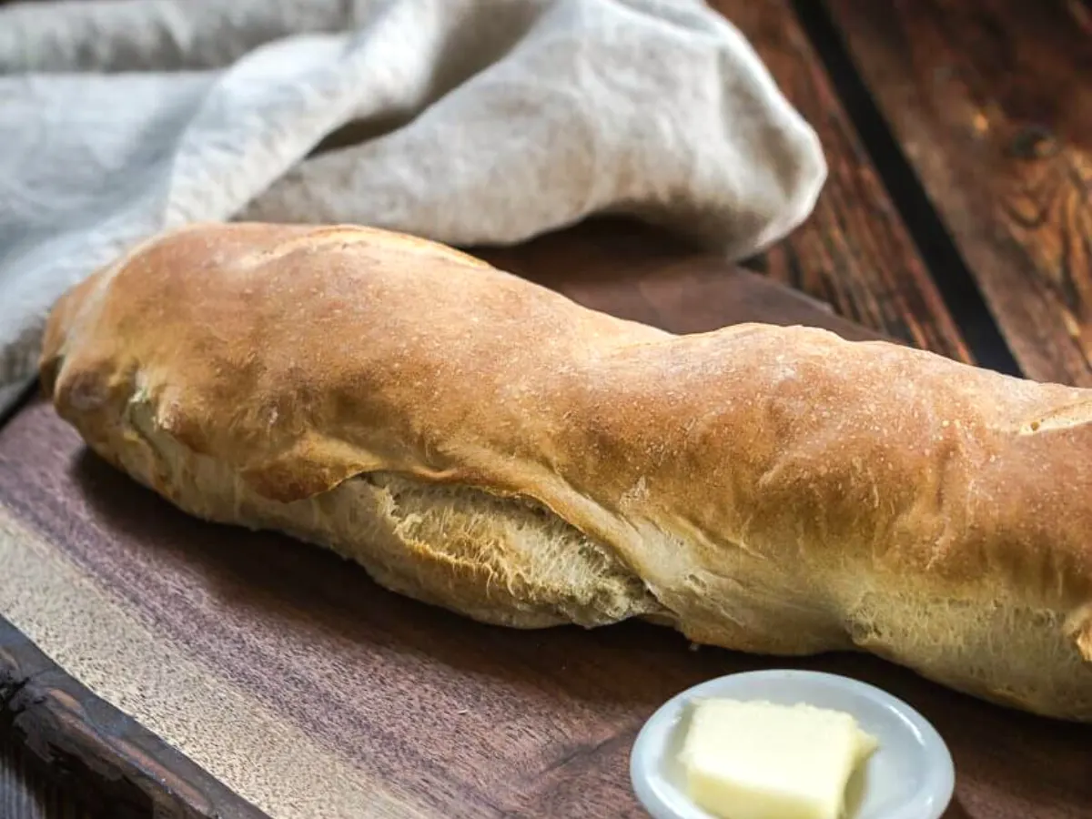 A crusty baguette of Italian bread sitting on a cutting board - Hostess At Heart
