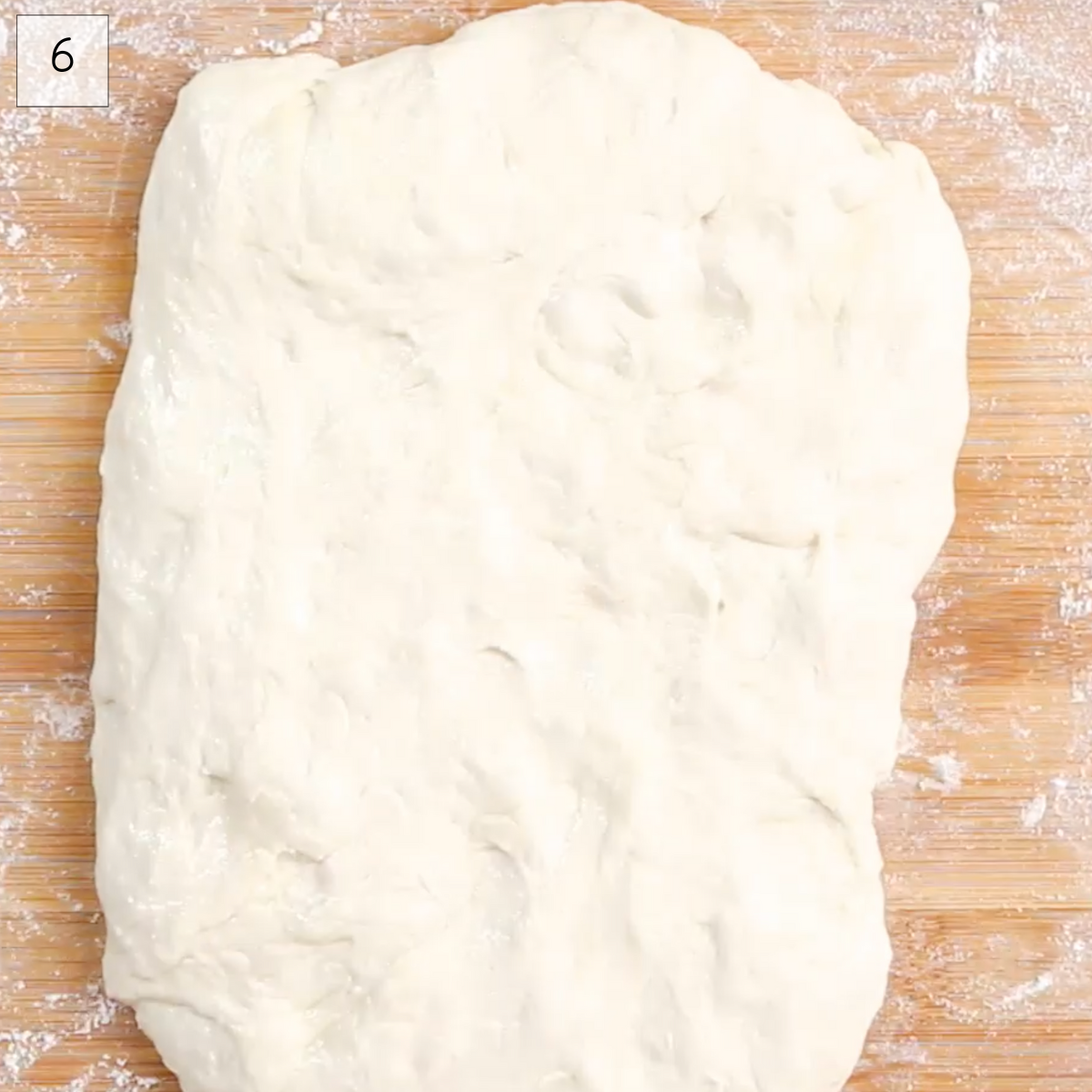 Top down view of bread dough shaped into a rectangle on a floured bread board.