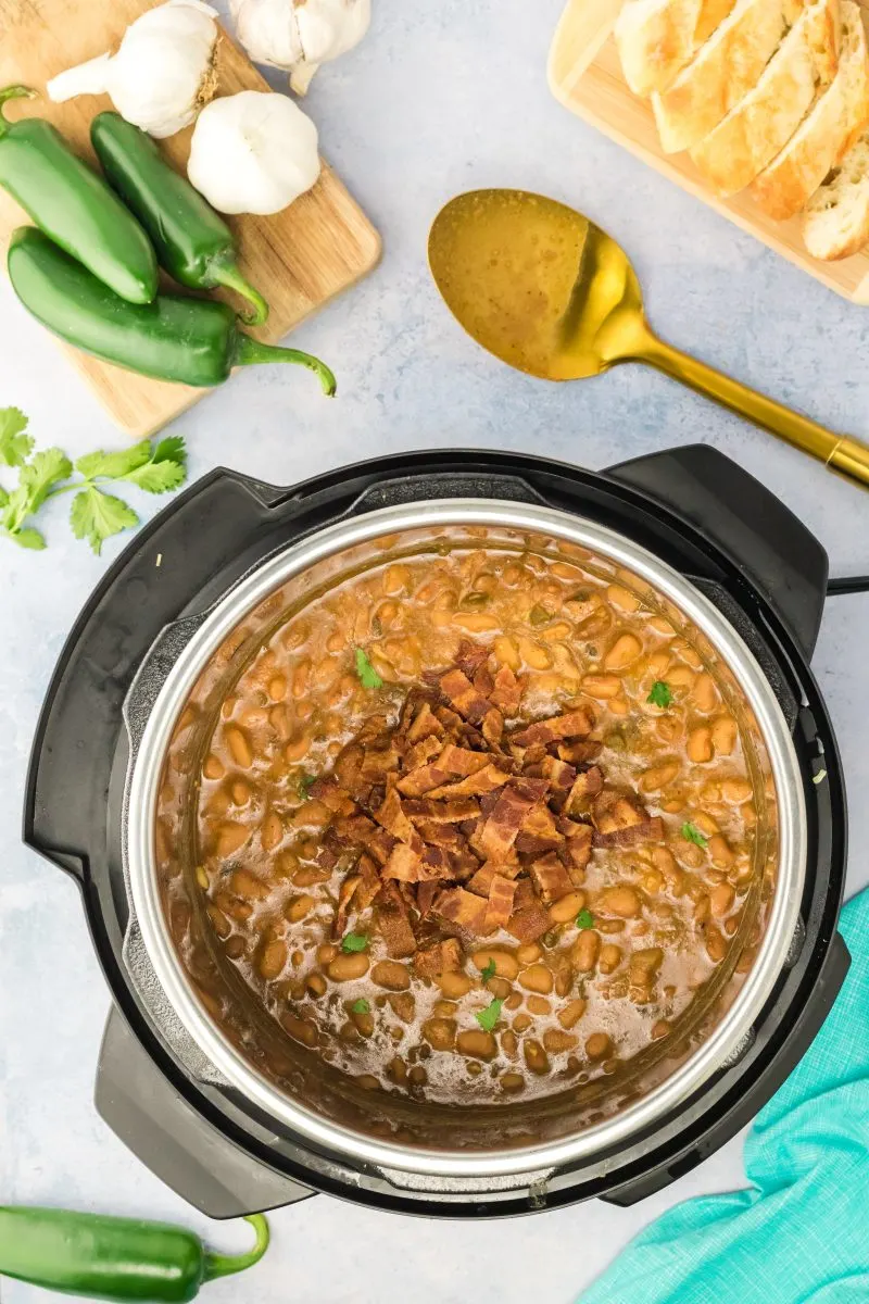 Top down view of an instant pot filled with cooked Charros beans topped with fresh cilantro and chopped bacon. Hostess At Heart