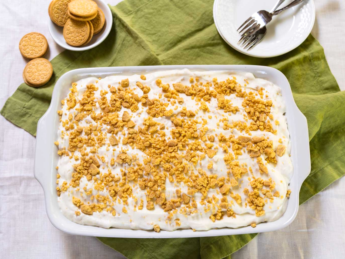 Top down view of a lemon poke cake topped with whipped cream and crushed cookies - Hostess At Heart