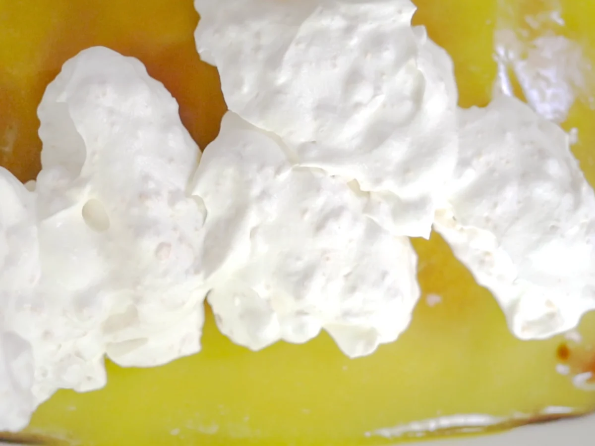 Top down biew of whipped cream being applied on top of a cake with lemon pudding glaze.