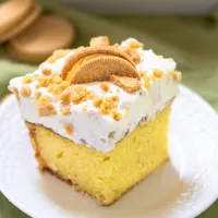 Angled view of a sliced piece of lemon cake topped with whipped cream and crushed cookies - Hostess At Heart