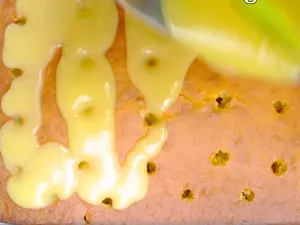 Top-down view of a baked lemon cake poked with holes and a lemon glaze being poured over the top - Hostess At Heart