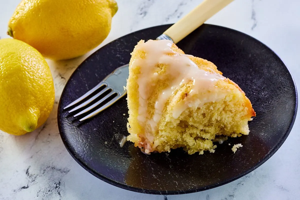 Angled view of a slice of moist lemon cake topped with lemon glaze on a plate - Hostess At Heart
