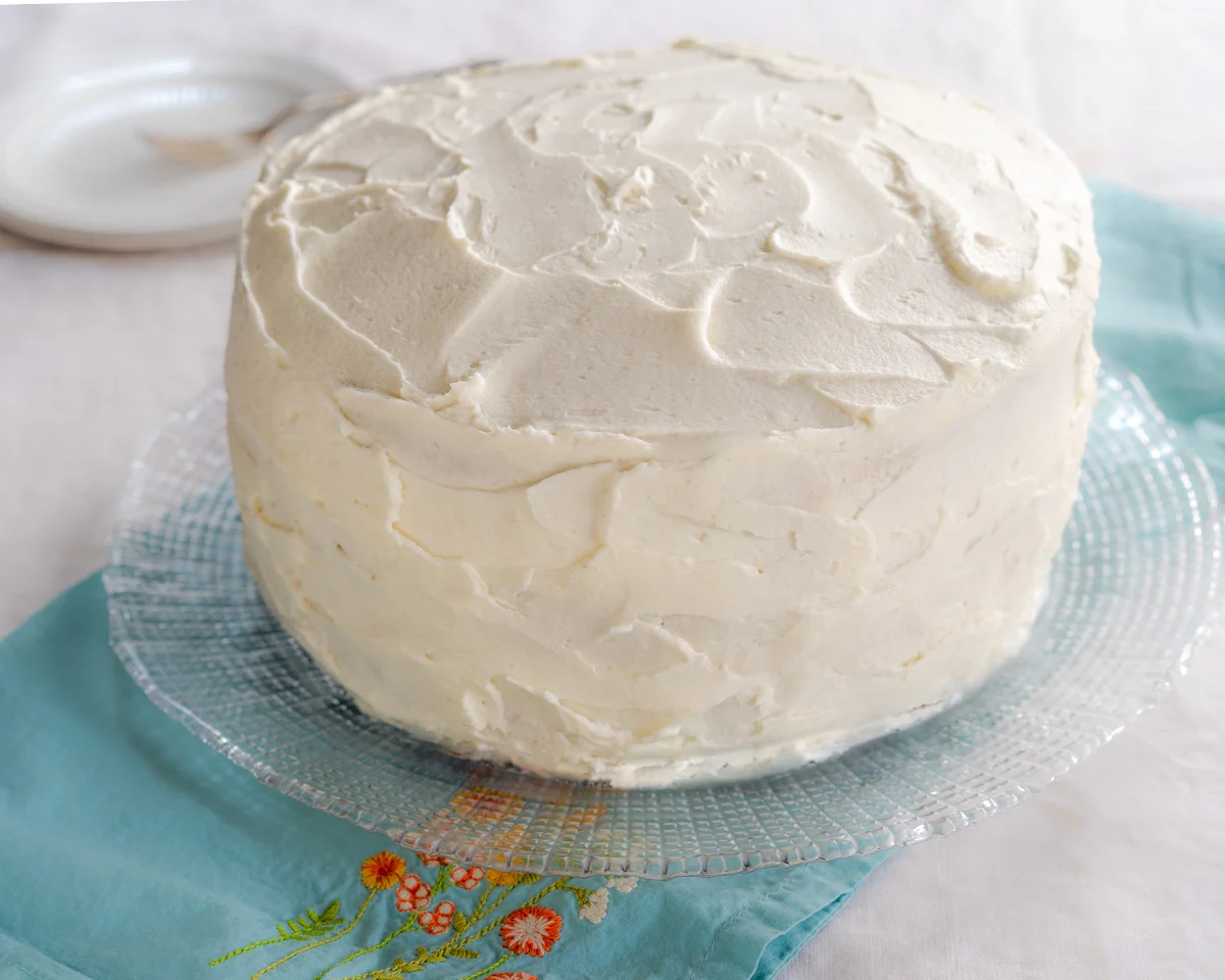 A whole classic vanilla cake sitting on a glass cake platter. - Hostess At Heart