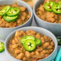 Angled view of a bowl of cooked Pinto beans topped with jalapeno pepper slices - Hostess At Heart