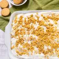 Top down view of a lemon poke cake topped with whipped cream and crushed cookies - Hostess At Heart