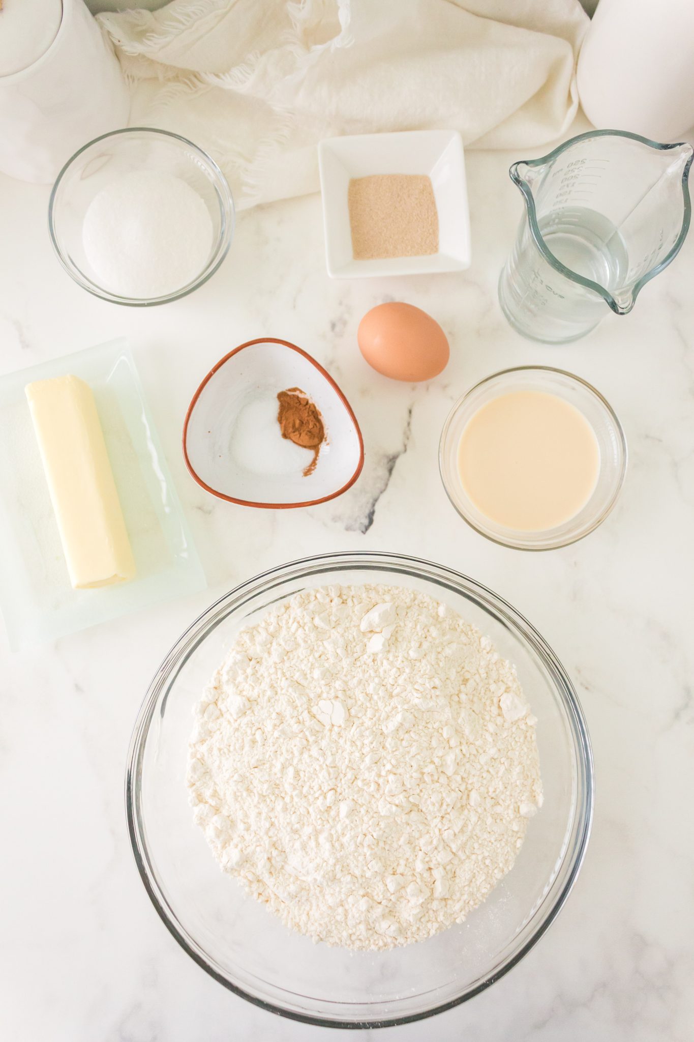 Top down view of the ingredients used to make Mexican Conchas including flour, butter, sugar, yeast, cinnamon, water, and evaporated milk - Hostess At Heart