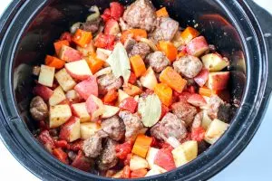 Top-down view of a crockpot filled with tomatoes, beef, carrots, tomatoes and a bay leaf - Hostess At Heart
