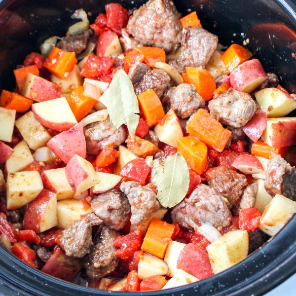 Top-down view of a crockpot filled with tomatoes, beef, carrots, tomatoes and a bay leaf - Hostess At Heart