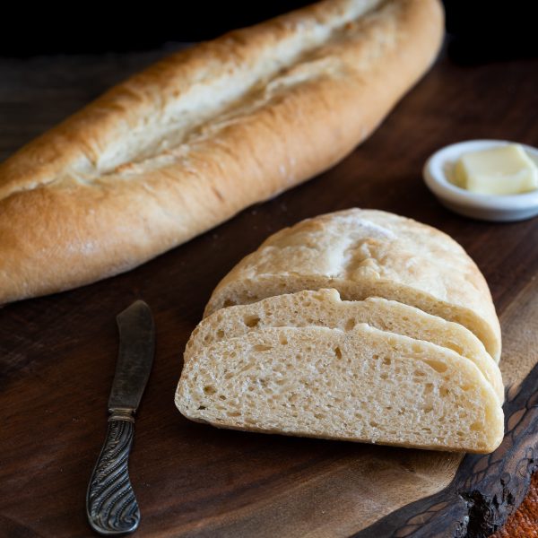 A sliced loaf of Cuban bread sitting on a cutting board in front of an uncut loaf - Hostess At Heart