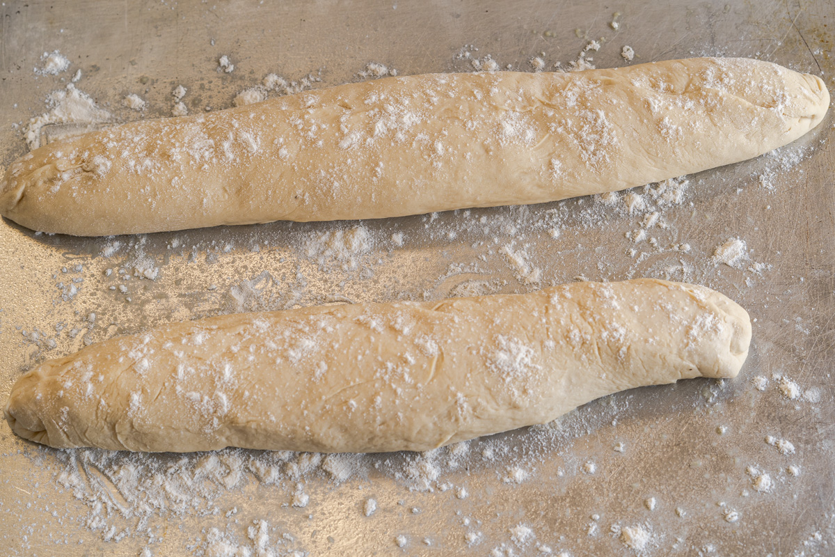 Two baguettes dusted with flour sitting on a baking sheet - Hostess At Heart