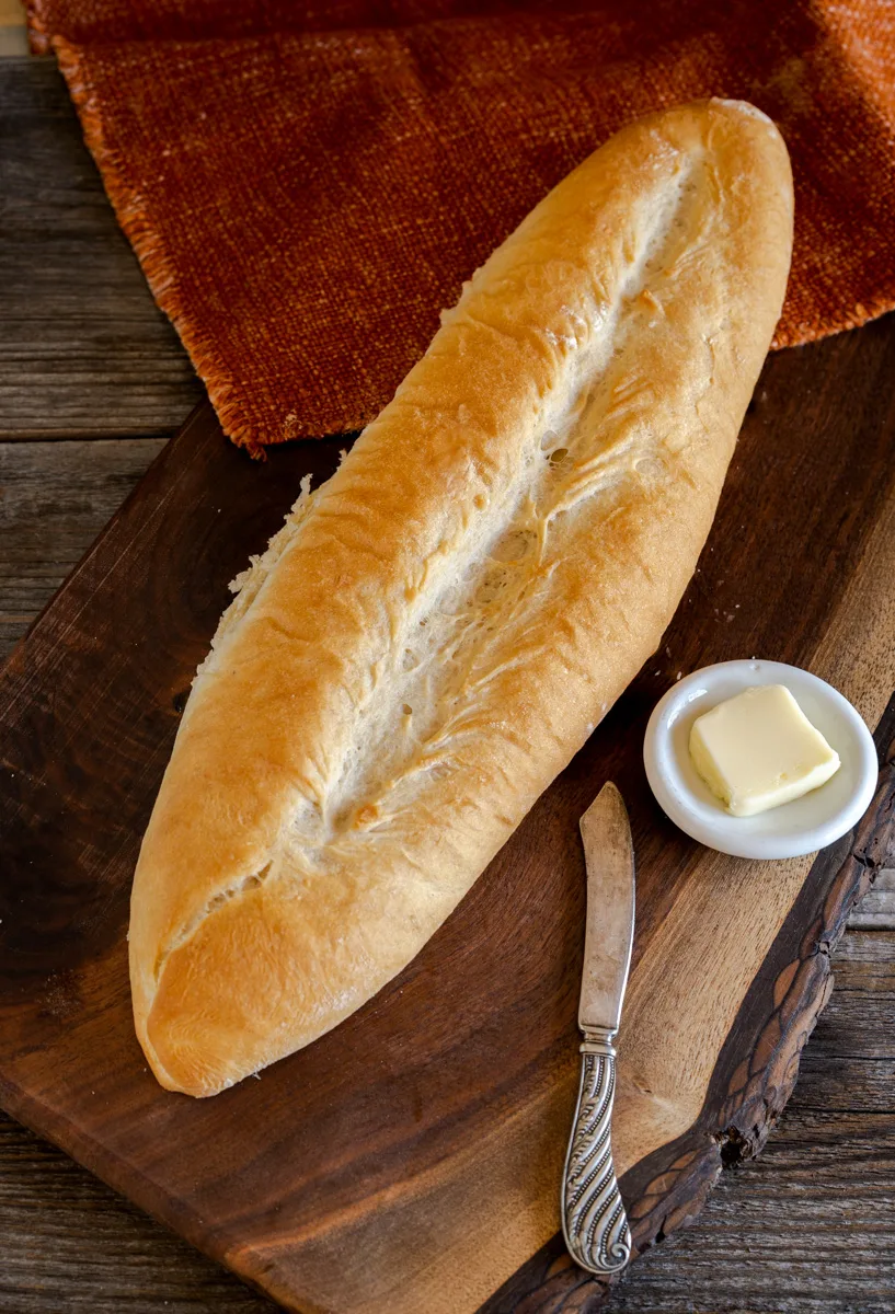 A bread baguette sitting on a cutting board next to a dish holding butter - Hostess At Heart