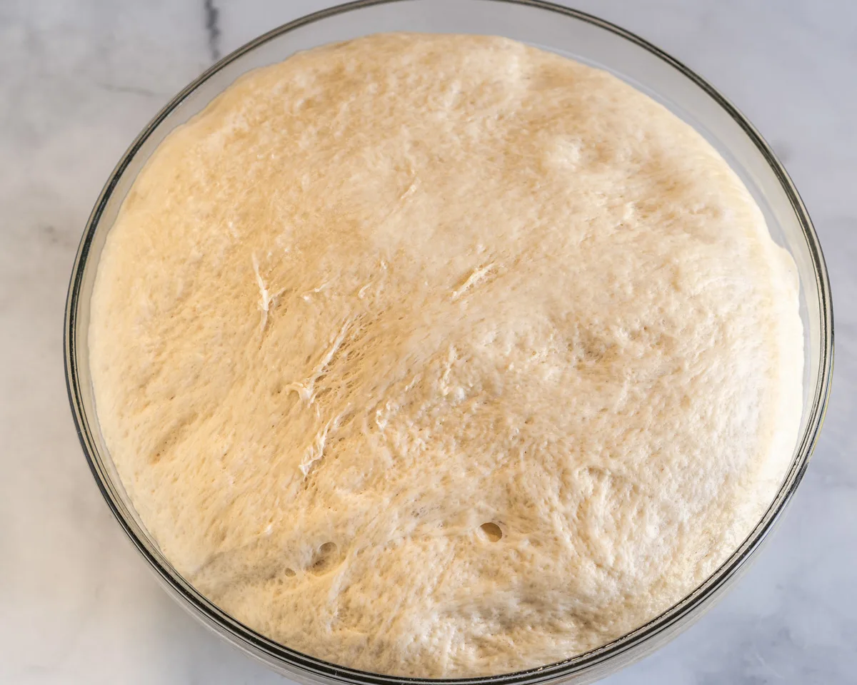 A glass bowl filled with proofed bread dough - Hostess At Heart