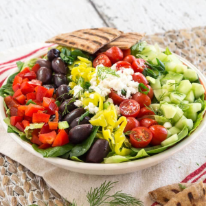 Angled view of a lettuce salad topped with healthy ingredients such as tomatoes, olives, peppers, cucumbers, and a lemon dressing - hostess at Heart
