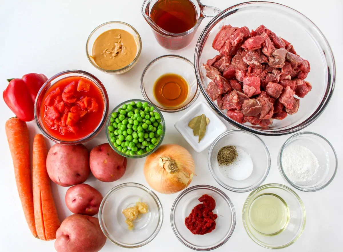 Top down view of the ingredients used in Korean stew including meat, potatoes, onion, garlic, tomatoes, red pepper, corn startch, and peanut butter.