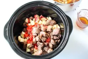 Top down view of a slow cooker filled with beef, potatoes, and tomatoes - Hostess At Heart