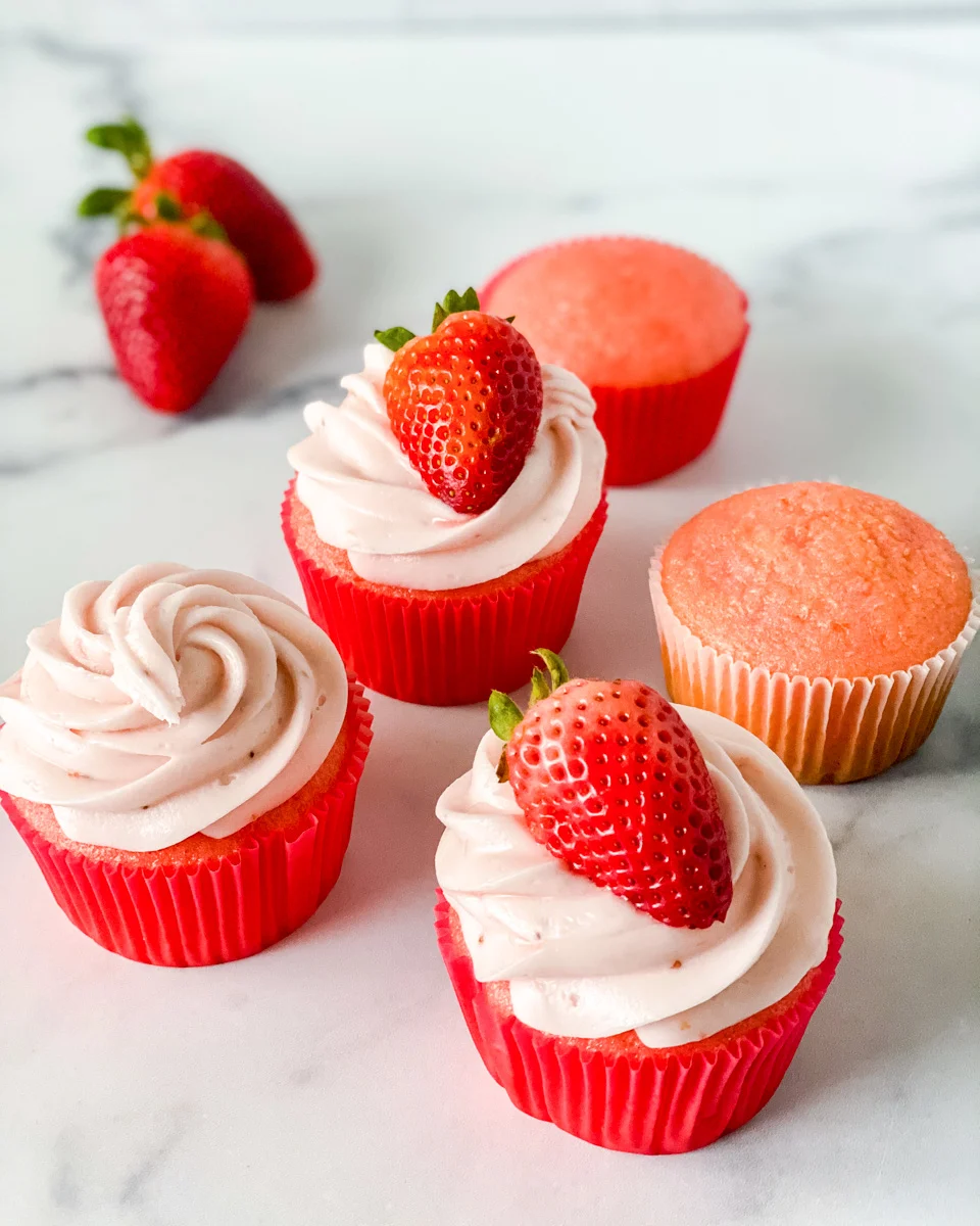 Angled view of pink cupcakes topped with pink frosting and a slice of a fresh strawberry - Hostess At Heart