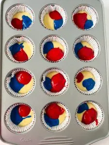 Top-down view of a muffin tin filled with dollops of red, white, and blue cupcake batter - Hostess At Heart