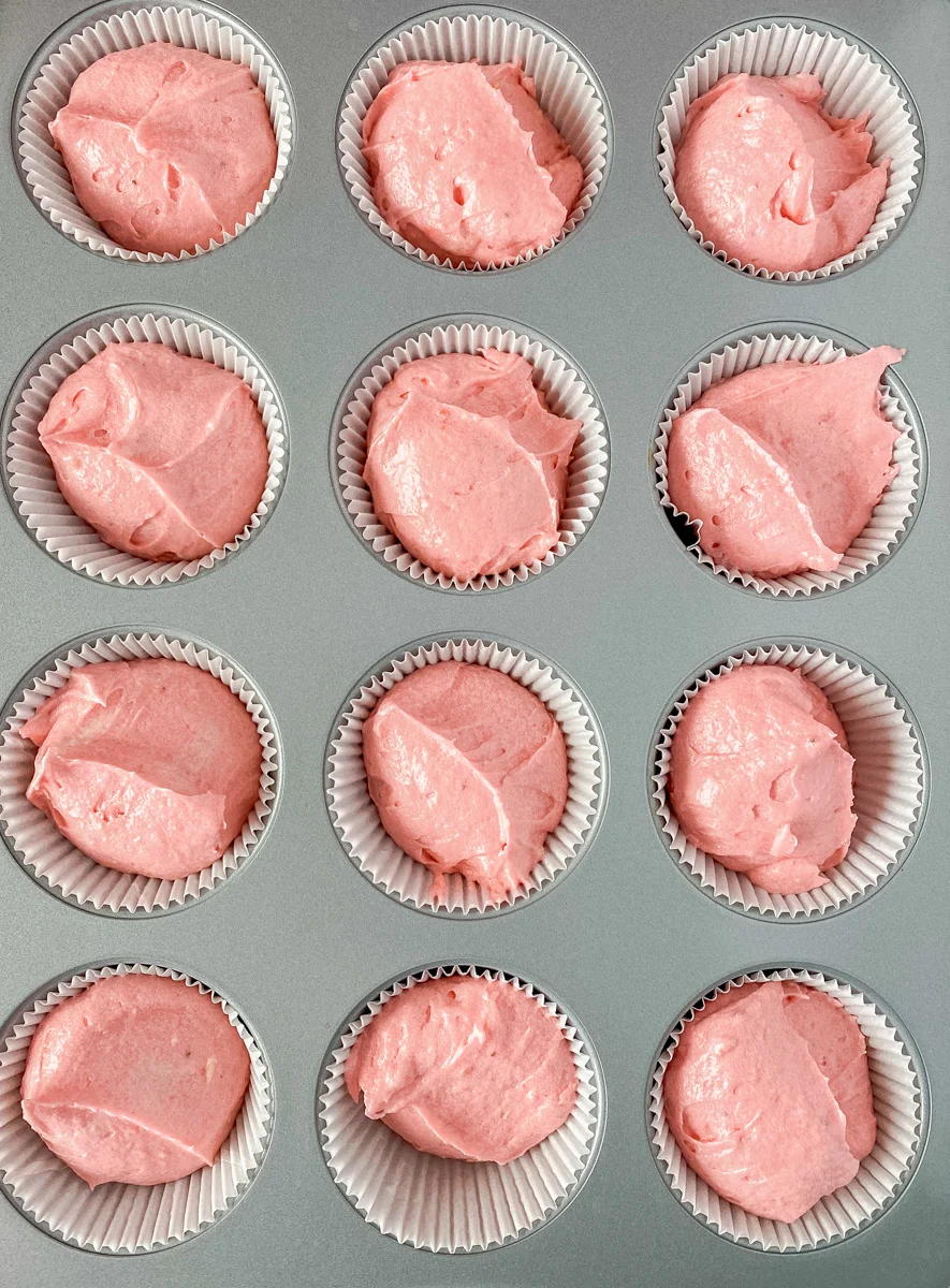 A cupcake pan filled with cupcake liners and filled with strawberry cake batter - Hostess At Heart