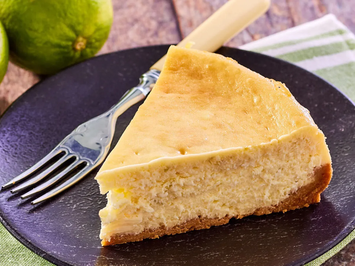 Angled sideview of a slice of Key Lime Cheese cake with a graham cracker crust sitting on a plate. Hostess At Heart