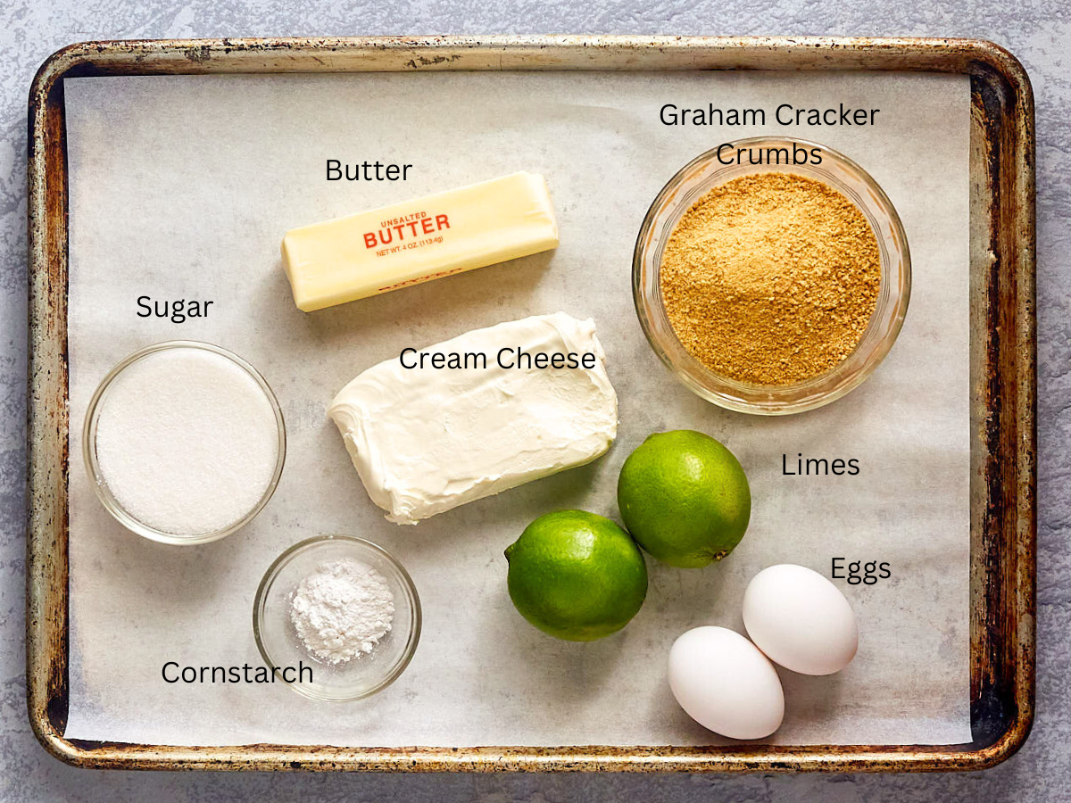Top-down view of the ingredients used to make a key lime cheesecake recipe including sugar, limes, eggs, cream cheese, and graham cracker crumbs.