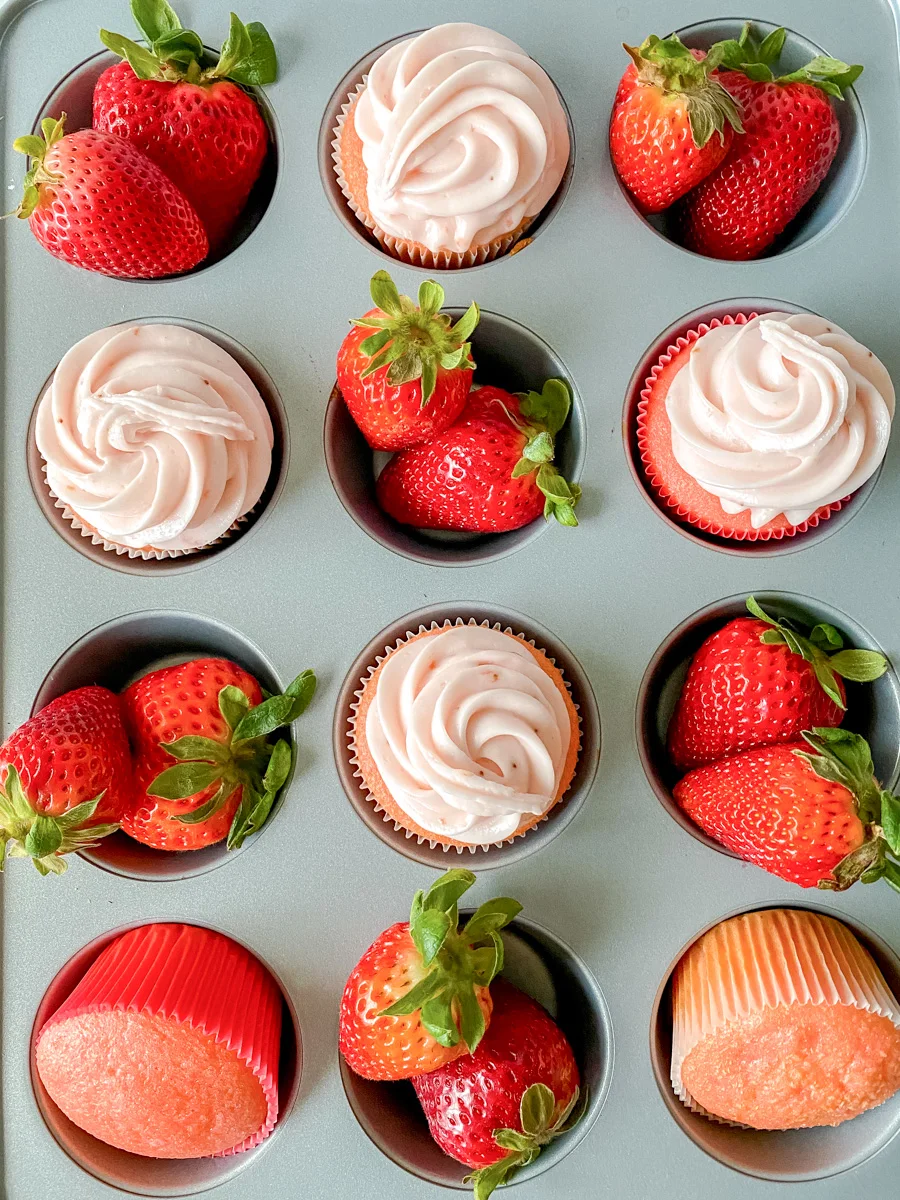 Top down view of a muffin tin filled with frosted and unfrosted strawberry cupcakes recipe alternating with fresh strawberries - Hostess At Heart