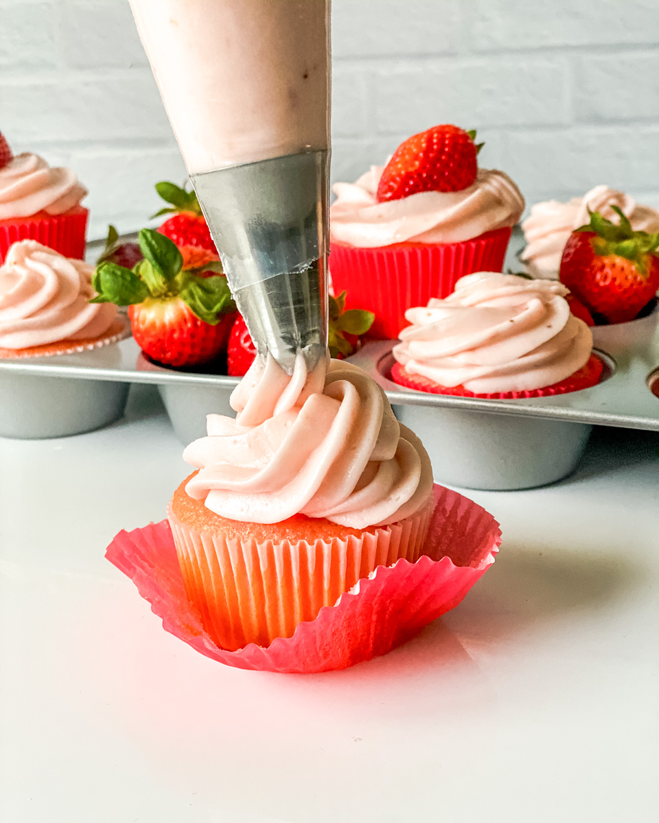 Sideview of a cupcake with frosting being piped from the top - Hostess At Heart