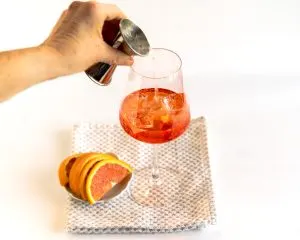 Club soda being added to a wine glass on top of aperil spritz ingredients. Hostess At Heart