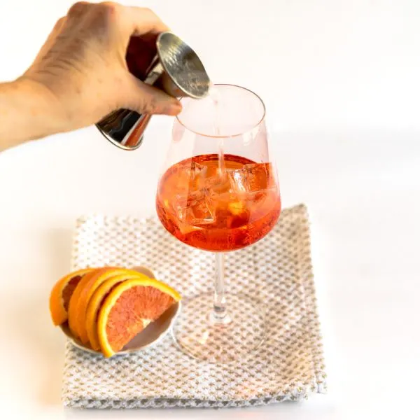 Club soda being added to a wine glass on top of aperil spritz ingredients. Hostess At Heart