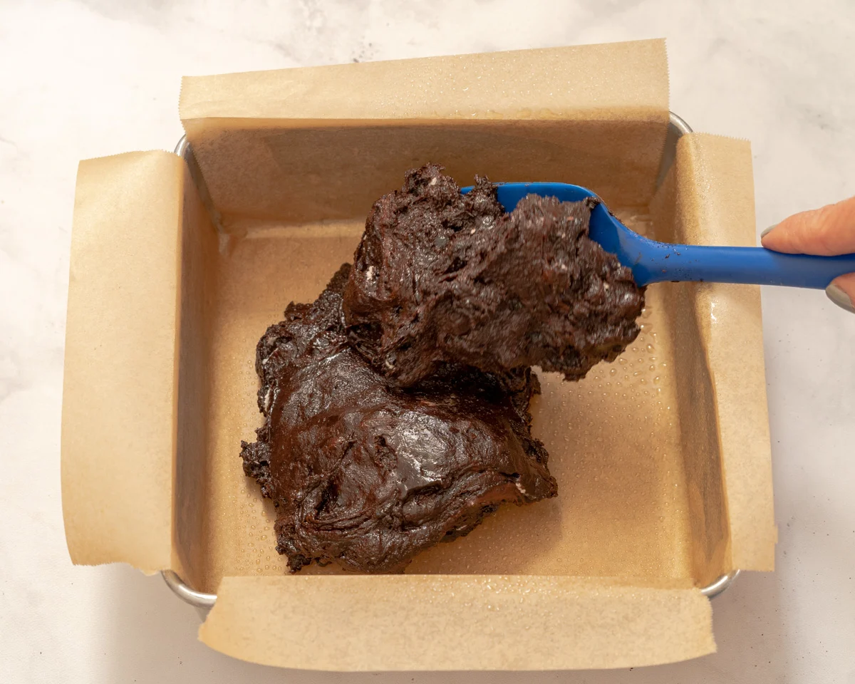 A parchment-lined baking pan filled with thick chocolate batter. Hostess At Heart