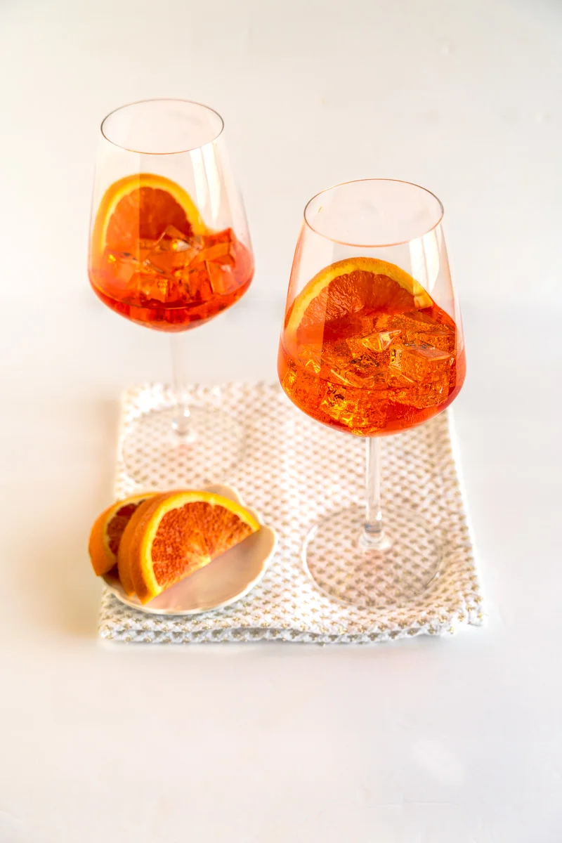 To glasses filled with orange hued Italian cocktail known as an aperol spritz cocktail. Hostess At Heart