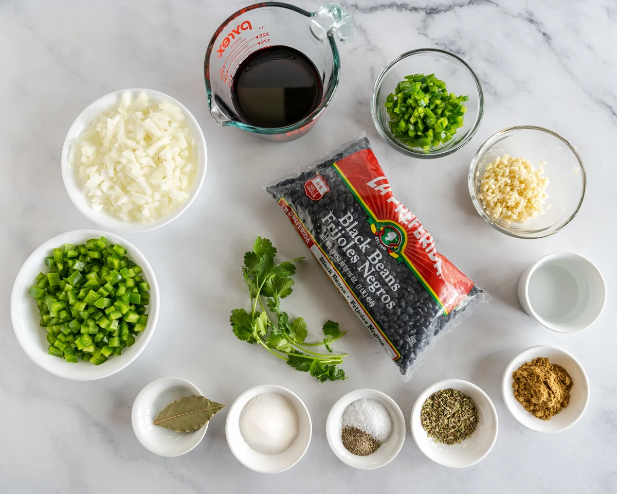 Top down view of ingredients including sliced green peppers, onion, jalapenos, minced garlic, fresh cilantro, dried black beans, spices, vinegar and wine.