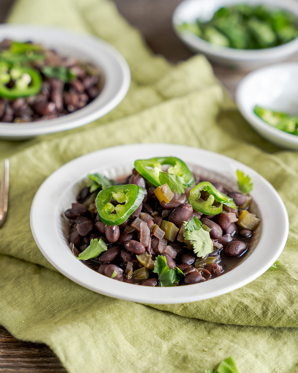 A side view of a bowl filled with black beans cooked with onion and jalapenos. Hostess At Heart