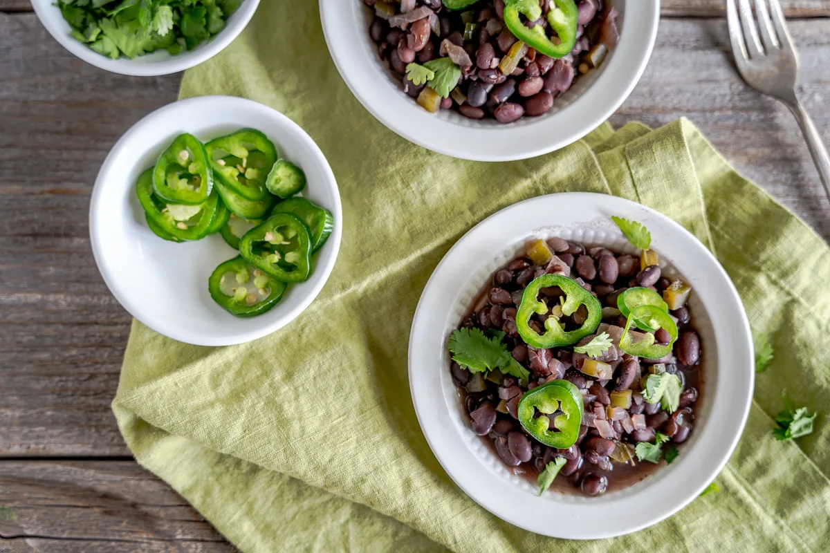Bowls of Cuban Black Beans Reciope garnished with cilantro and jalapenos - hostess at heart