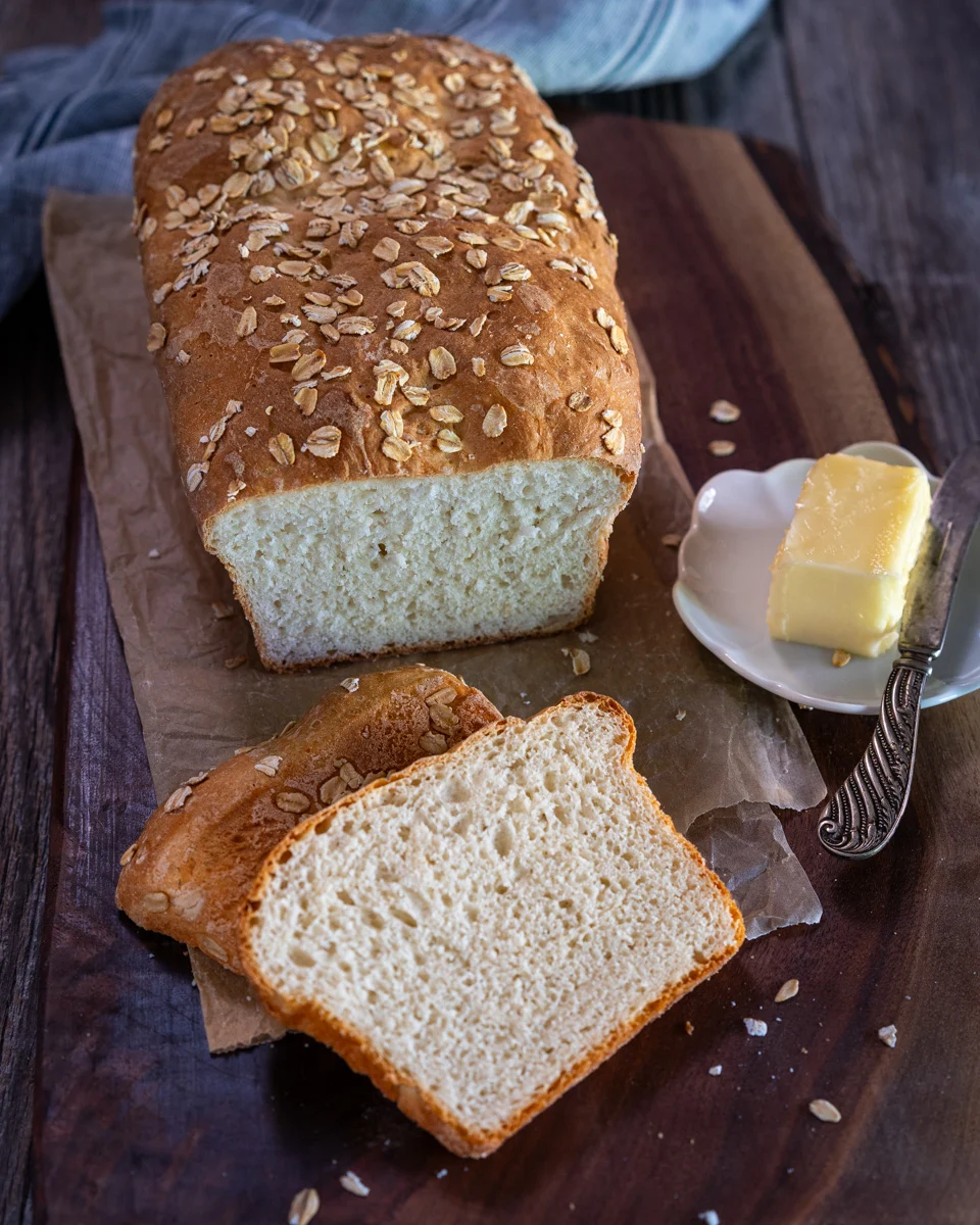 Top down view of a loaf of bread topped with oats with the front two slices cut an laying in front of the loaf. Hostess At Heart