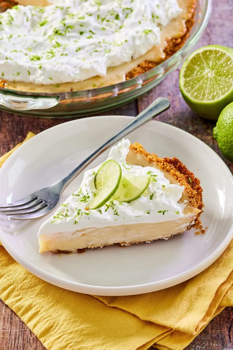 Angled view of a slice of creamy keylime pie with graham cracker crust. The sliced pie is in the background - Hostess At Heart