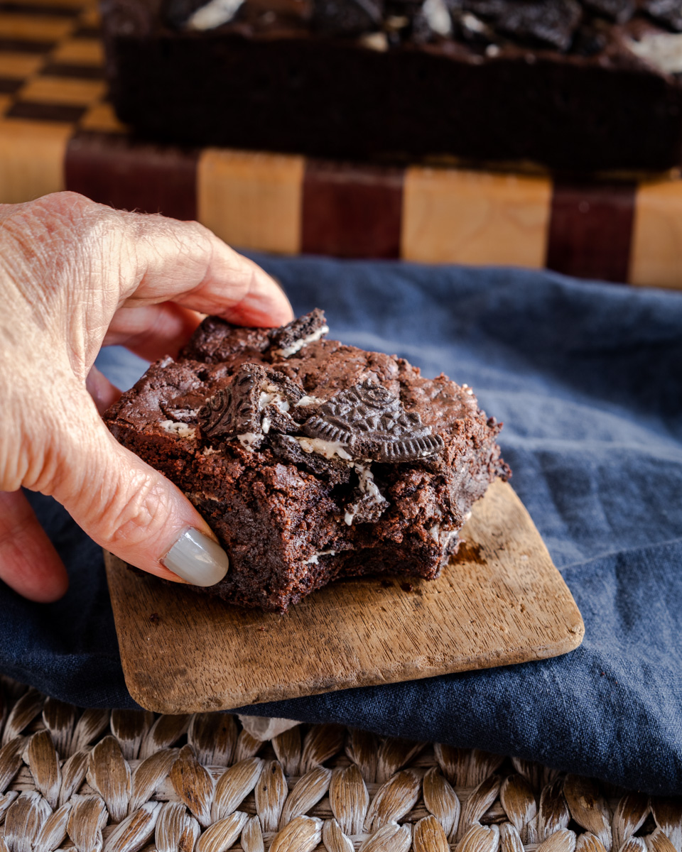 A hand grabbing a chocolate Oreo Brownie with a bite taken out of it. - Hostess At Heart
