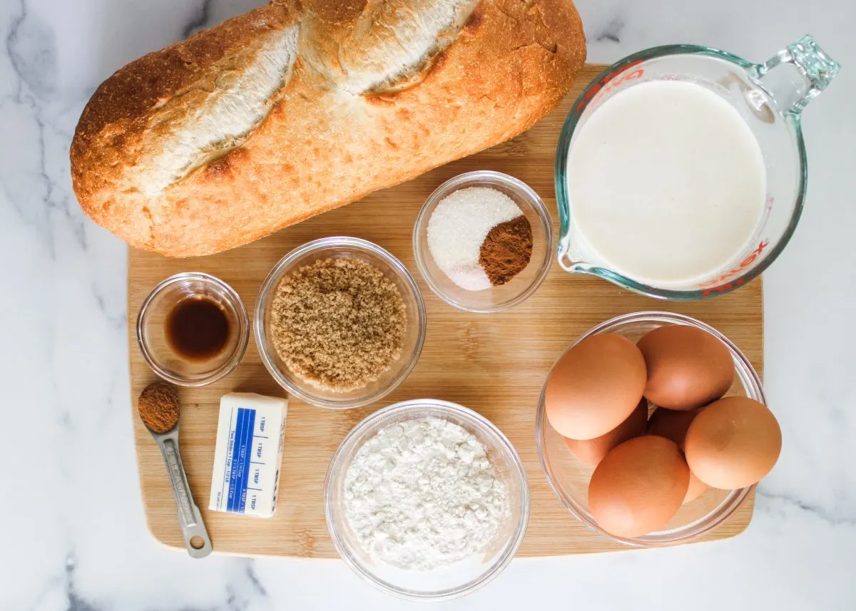 Top down view of the ingredients used to make French Toast Muffins including bread, vanilla, cinnamon, butter, brown sugar, eggs, flour, milk, and flour.
