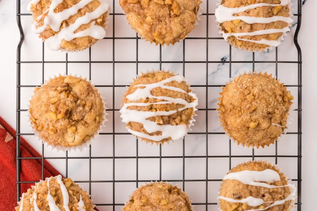 Top down view of apple crumble muffins sitting on a cooling rack with half of them drizzled with glaze.