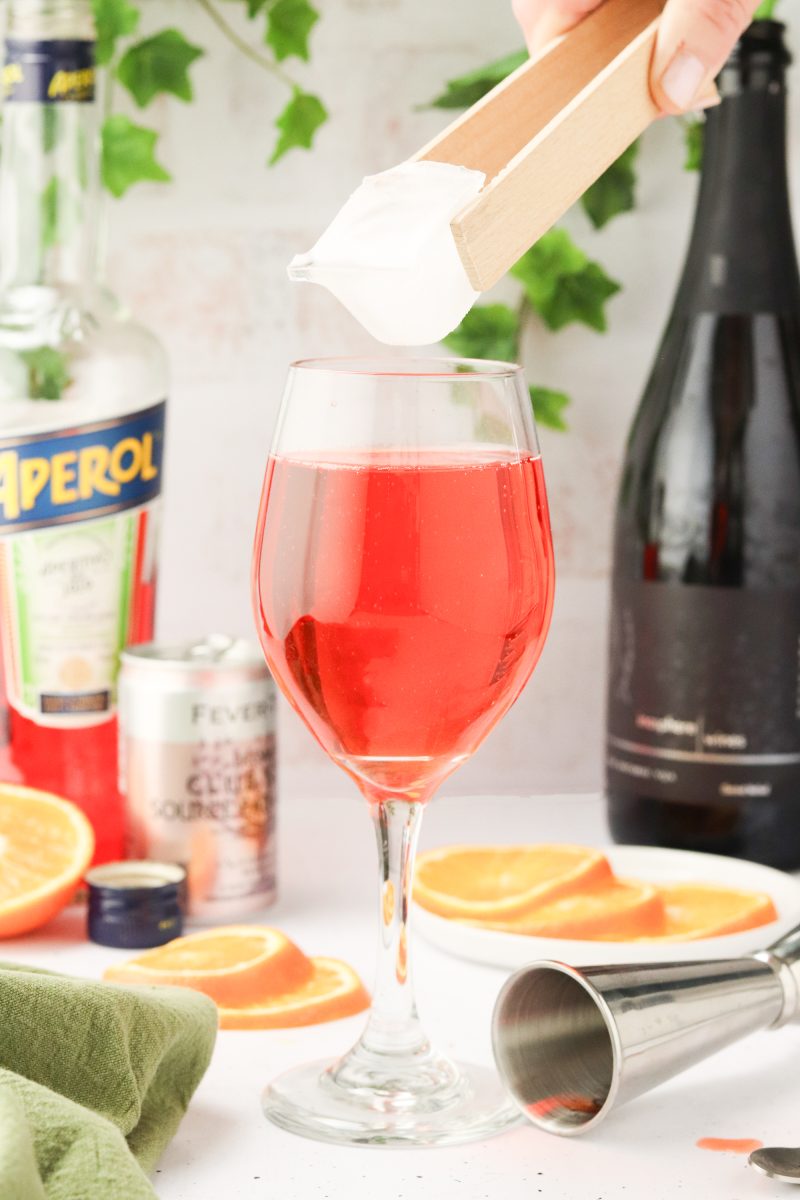 An ice cube hovering over a cocktail glass filled with an aperol cocktail. Hostess At Heart