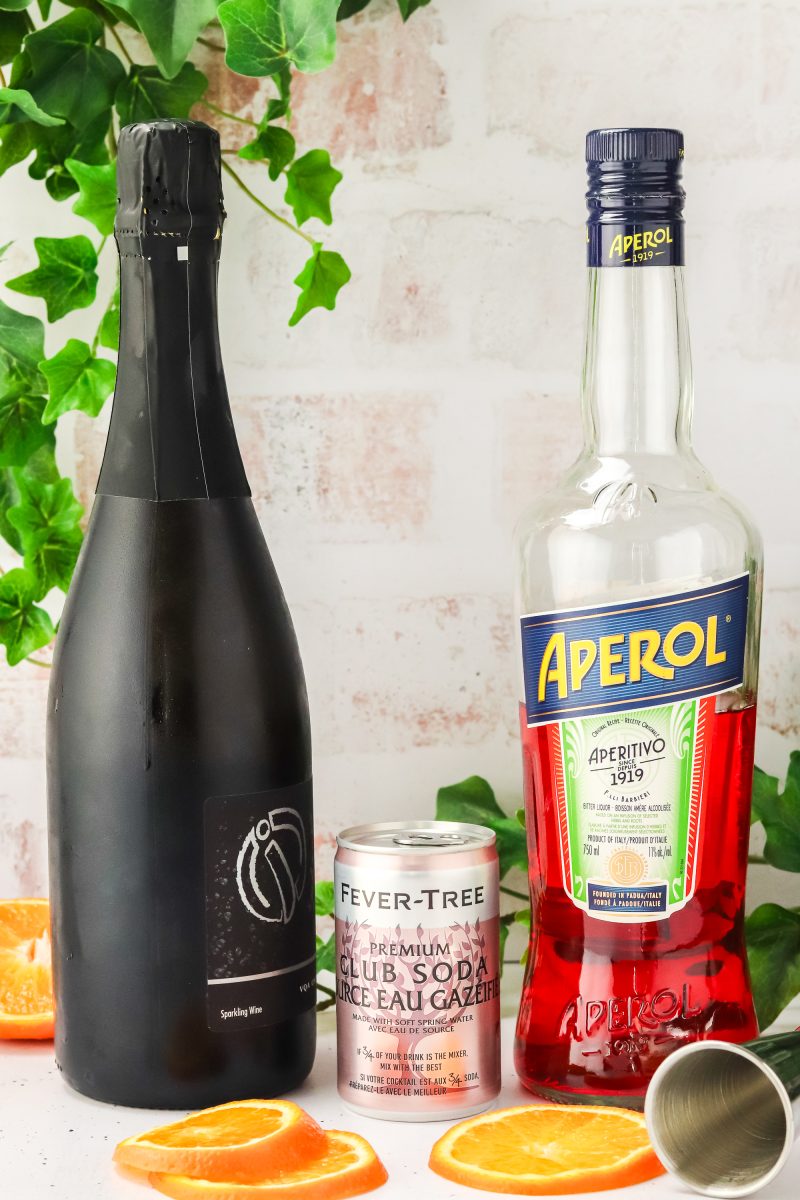 Ingredients used aperol spritzers including prosecco, aperol, and club soda next to two glasses of ice.