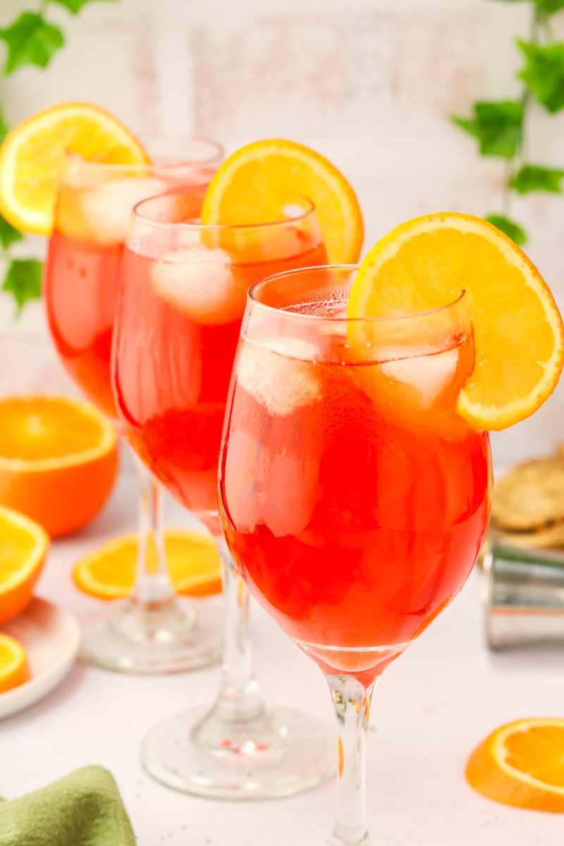 Sideview of three Aperol cocktails lined up and garnished with a orange wheel. Hostess At Heart